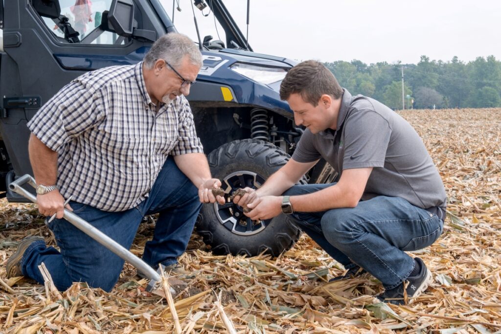 Farmers examine soil in corn field.