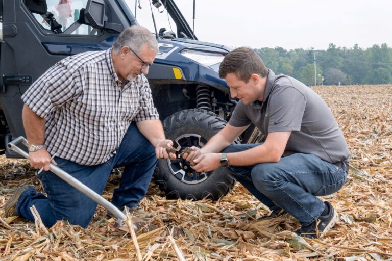 Farmers examine soil in corn field.
